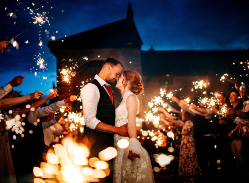 Bride and Groom Look Into Each Others Eyes as Sparklers Light Behind Them