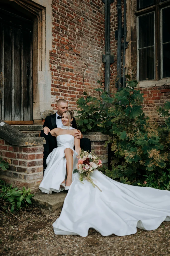 Tiffany and Dan on the brick steps at Doddington Hall with her dress spread out