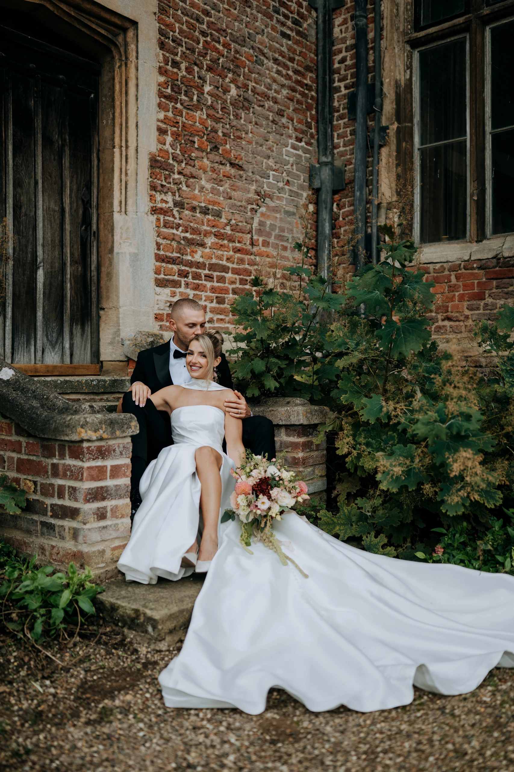 Tiffany and Dan on the brick steps at Doddington Hall with her dress spread out